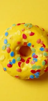 Bright yellow donut with colorful sprinkles on yellow background.