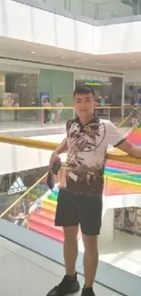 A person stands by a railing inside a modern mall with colorful stairs.