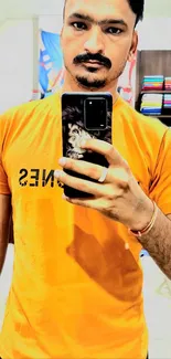 Mirror selfie with bright orange t-shirt showcasing modern fashion.