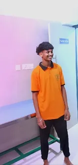 Young man in orange shirt in a pastel-lit modern room.