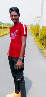 Person in red shirt standing on a road flanked by greenery.