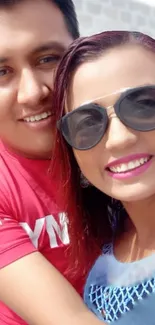 A couple posing happily for a selfie with bright smiles and sunglasses.