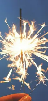 Sparkler in hand glowing against a blue night sky.