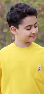 Young boy in bright yellow shirt with natural backdrop.