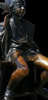 Bronze statue of seated figure against a black background.