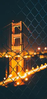 Golden Gate Bridge glowing at night through a fence.