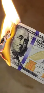 A burning hundred-dollar bill with flames and smoke.