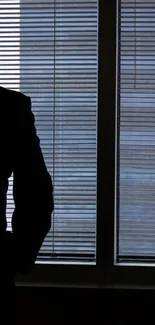 Silhouette of a person looking out an office window with blinds.