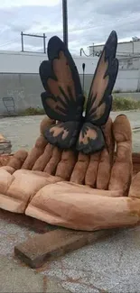 Wooden hands sculpture with butterfly wings in urban setting.