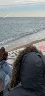 Person relaxing on a graffiti-adorned beach wall by the ocean.