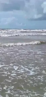 Calming ocean waves on a cloudy day, offering a serene beach view.