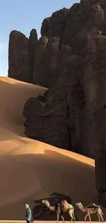 Camel caravan crossing desert dunes alongside rocky cliffs.