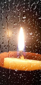 Candle flame glows behind rain-covered glass wall.