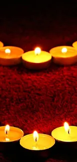 Romantic candlelit heart arrangement on a dark red surface.