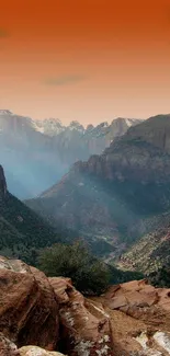 Sunrise over a majestic canyon with orange sky and rugged terrain.