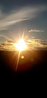 Stunning sunset horizon with sun rays and clouds in a dark blue sky.