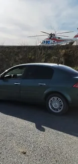 Gray car parked by roadside with helicopter in the sky.