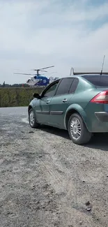 Green car and helicopter on gravel road wallpaper.