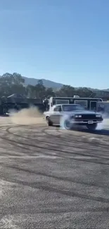 Classic car drifts on pavement with mountains and blue sky.