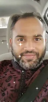 Man in car wearing maroon shirt, smiling.