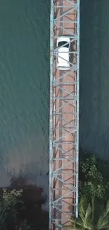 Aerial view of a car on a bridge over teal waters.