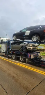 Car transporter truck on a wet road under a cloudy sky with vibrant vehicles.