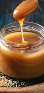 Caramel sauce dripping from spoon into jar on wooden tray.