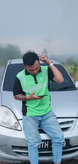 Person in green shirt leaning against a silver car.