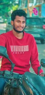 Man in red sweater on black motorcycle outdoors.