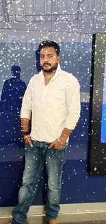 Man in white shirt and blue jeans standing casually against a blue background.