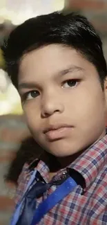 Young boy in checkered shirt, brick background.