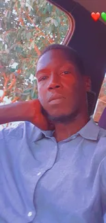 Casual portrait of a man sitting in a car with a scenic tree background.