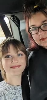 Two people taking a selfie inside a moving car.