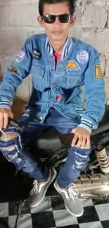 Man in denim on a motorbike against wall.