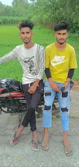 Two young men posing with a motorbike in a park.