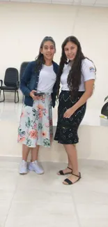 Two women in floral skirts pose stylishly indoors.