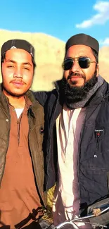 Two friends posing outdoors in casual outfits under a clear sky.