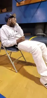 Person in casual wear sitting indoors on a chair in a gym setting.