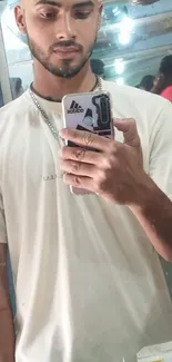 Casual young man taking a mirror selfie in a beige shirt.