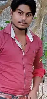 Man in red shirt posing outdoors with trees and nature background.