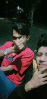 Two friends in casual attire sitting outdoors at night.