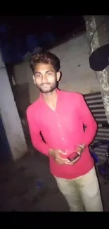 Man in red shirt poses in urban street at night.