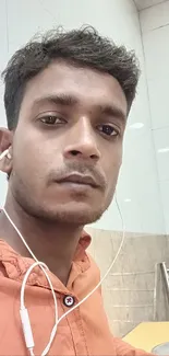 Portrait of a young man in an orange shirt with earphones.