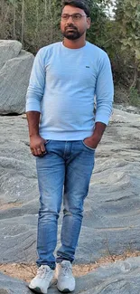 Man in blue jeans and sweater outdoors on rocks.