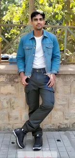 Man in denim jacket poses outdoors in a casual setting.