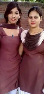 Two women in brown outfits posing outdoors.