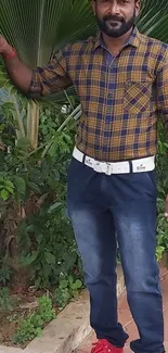 Man in plaid shirt with jeans standing outdoors.