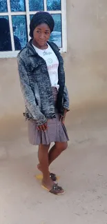 Woman in denim jacket and skirt standing outside.