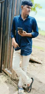 Young man in blue shirt holding a phone outdoors.