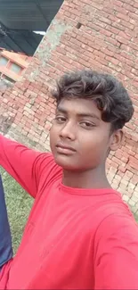 Young individual in red shirt with brick background.